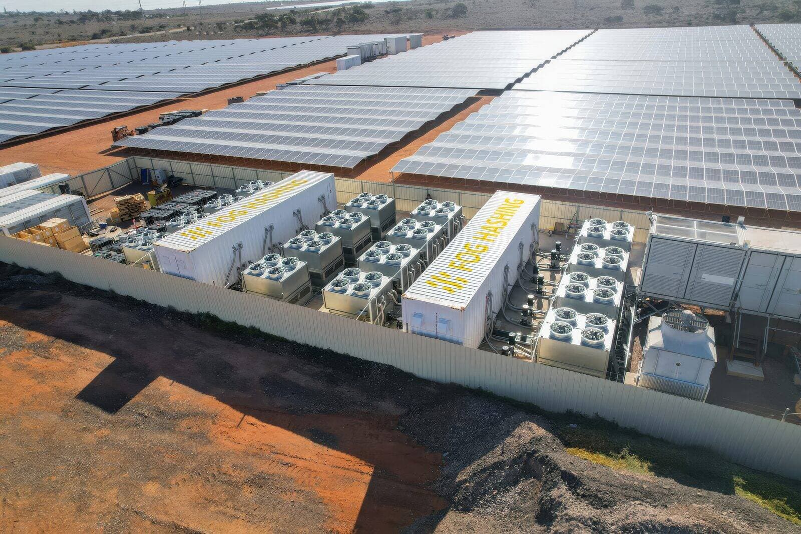 Aerial view of Fog Hashing immersion-cooled mining containers operating beside a large solar array on red outback soil.